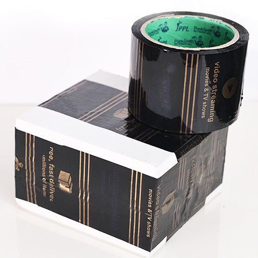 Printed packaging tape for Amazon sellers 3 inch x 65 m, black roll resting on a box sealed with the tape